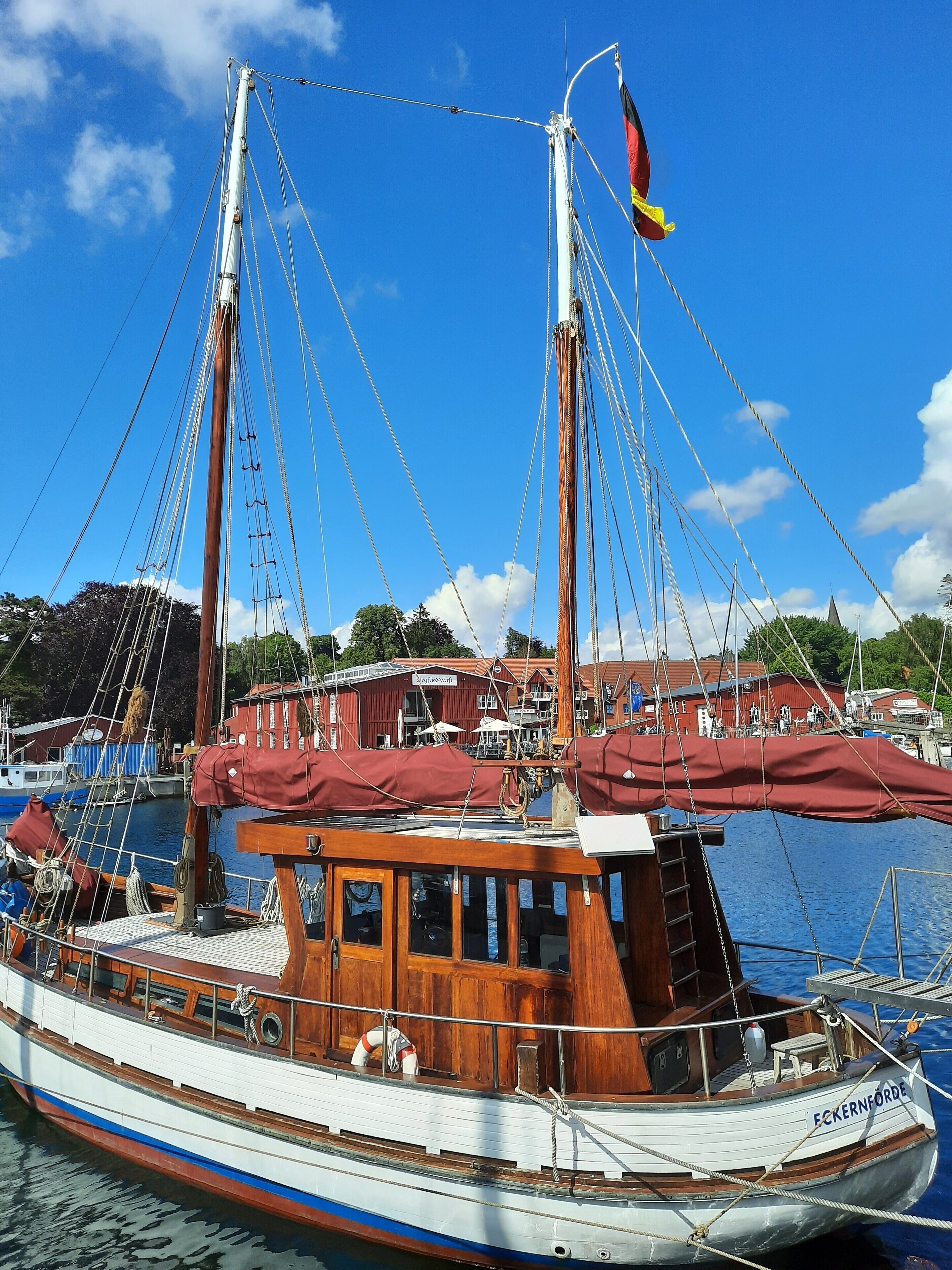 A traditional wooden boat docked at a marina with a clear blue sky and a building in the background.
