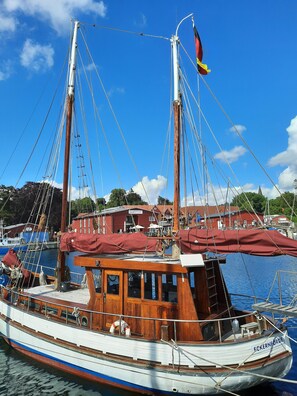 A traditional wooden boat docked at a marina with a clear blue sky and a building in the background.
