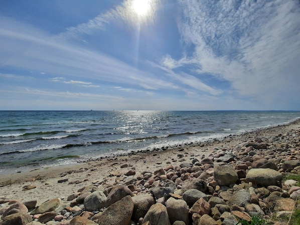 Ein felsiger Strand mit Wellen, einem klaren Himmel und strahlender Sonne.
