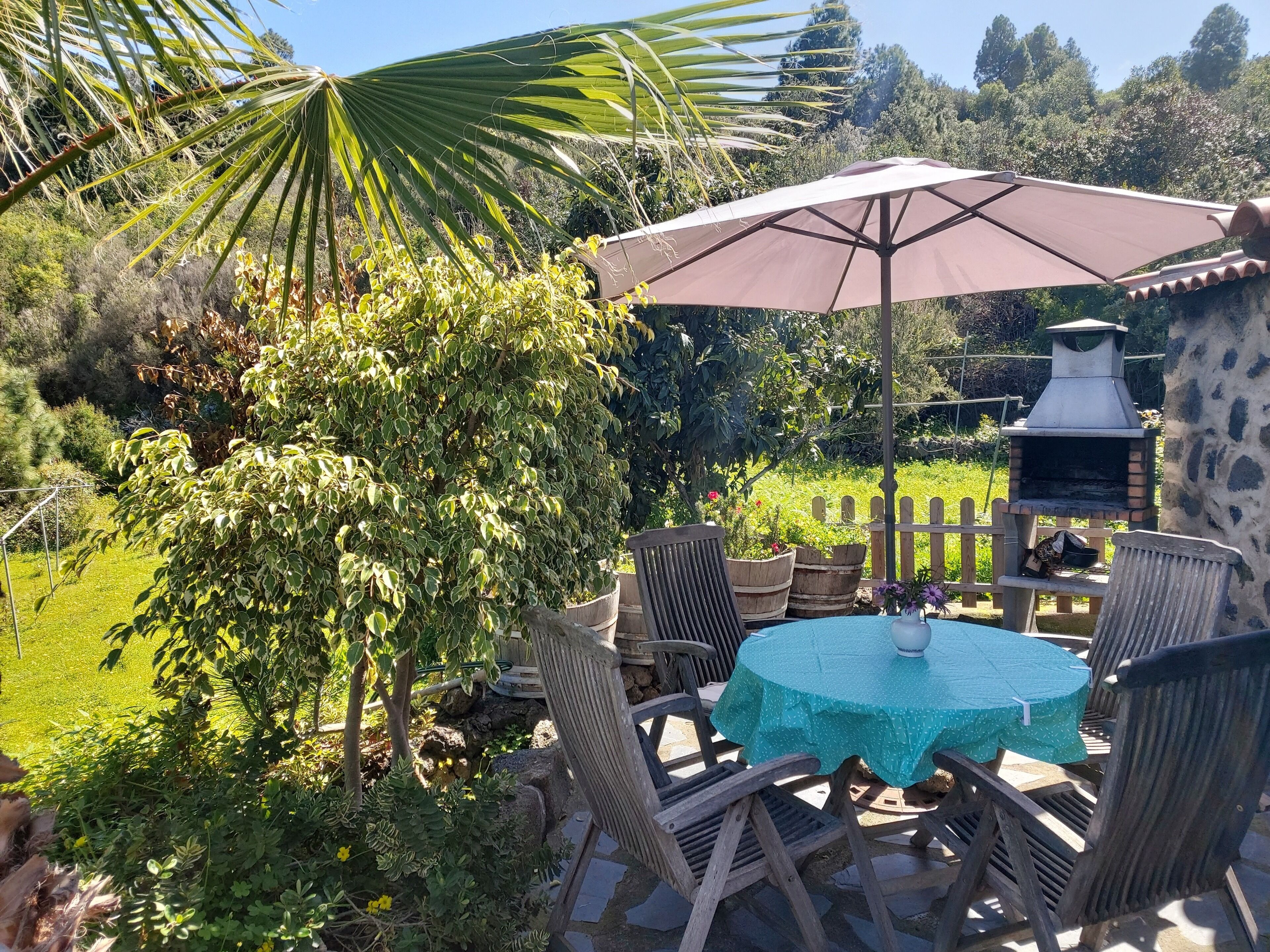 A patio with a round table and chairs, a large umbrella, and a stone barbecue grill.
