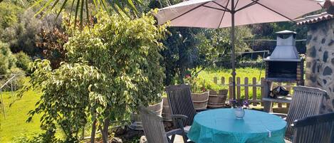 A patio with a round table and chairs, a large umbrella, and a stone barbecue grill.
