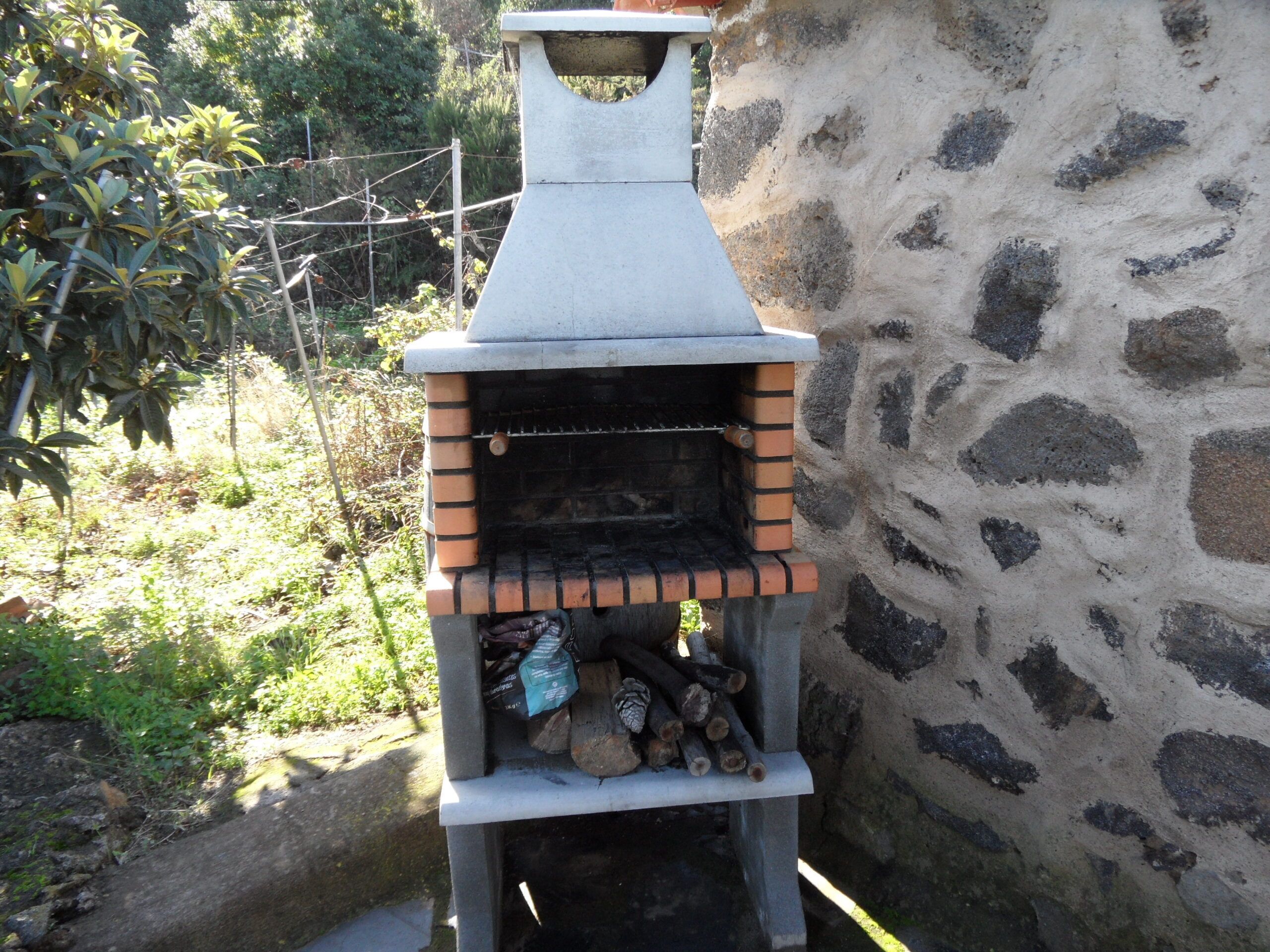 A stone-built outdoor oven with a brick base, surrounded by greenery and a stone wall.