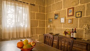 Un coin repas avec une table en bois, des chaises, un panier de fruits, une bouteille de vin et des tableaux encadrés accrochés au mur.