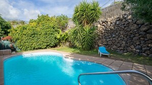 Une piscine entourée d’un mur en pierre et de verdure.