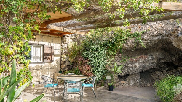 Une terrasse avec un mur en pierre, une table avec des chaises et diverses plantes.