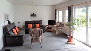 A living room with a black sofa, a wicker chair, a television, and a potted plant. - Just go on vacation. Vacation apartment 2-4 pers. 65sqm, terrace, 2 bedrooms. W-lan (Walkenried)