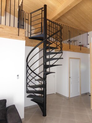 A modern spiral staircase with a wooden ceiling and a white door in the background.
