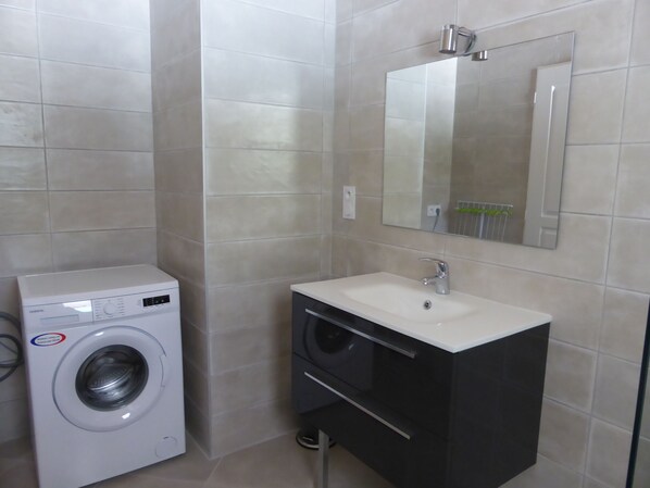 A compact bathroom with a washing machine, a sink, and a mirror.
