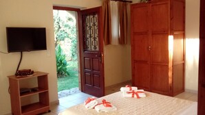 Una habitació amb un llit, un televisor penjat a la paret, un armari de fusta i una porta que dona a un jardí.