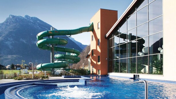 Una piscina con tobogán y montañas al fondo.