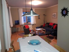 A cozy living room with a dining table, chairs, a sofa, and a TV.