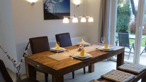A dining area with a wooden table, four chairs, a bench, and a painting on the wall. - Holiday house of high quality and cozy, sauna, 150m to the beach, quiet natural location (Rankwitz (OT Quilitz))