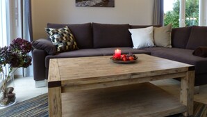 A living room with a dark brown sofa, a wooden coffee table with a candle, and a painting of a beach scene on the wall. - Holiday house of high quality and cozy, sauna, 150m to the beach, quiet natural location (Rankwitz (OT Quilitz))