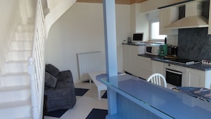 A modern kitchen with a microwave, coffee maker, and a gas stove. There is a dining table with a chair and a sofa in the living area.