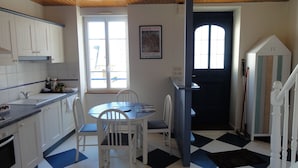 A kitchen with white cabinets, a dining table with chairs, a window, and a door with a number.