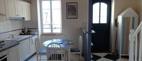 Cozinha com armários brancos, mesa de jantar com cadeiras, janela e porta com um número.