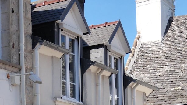 A two-story building with a blue door, a small balcony, and a stone staircase leading to the entrance.