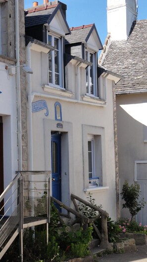 A two-story building with a blue door, a small balcony, and a stone staircase leading to the entrance. - Holiday house in the village of CARANTEC (Carantec)