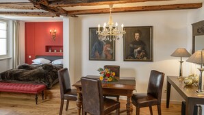 Une pièce comprenant une table à manger en bois, quatre chaises, un lustre et un lit avec une tête de lit rouge.