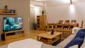 Olohuone, jossa on televisio, sohva ja sohvapöytä sekä ruokailutila, jossa on pöytä ja tuolit.