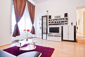 Ein modernes Wohnzimmer mit einem Glastisch, einem violetten Teppich und einer TV-Konsole mit Regalen.