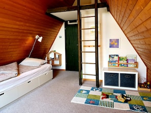 A cozy attic bedroom with a loft bed, a ladder, a bookshelf with children's books, and a colorful rug.