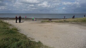 A sandy beach with people and a stroller, a grassy area, and a body of water in the background. - Family-friendly holiday house with large garden and great features (Butjadingen-Burhave)