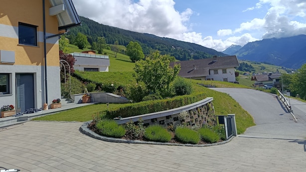A residential area with a curved driveway, a stone wall with plants, and houses with sloped roofs. - Guesthouse Michael in Navis am Brenner - Valley of Love (Navis)