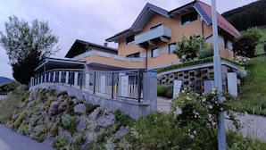 A modern two-story building with a balcony, a stone retaining wall, and a sign indicating a business or educational facility. - Guesthouse Michael in Navis am Brenner - Valley of Love (Navis)