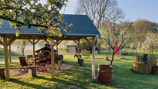A covered patio with a grill, outdoor seating, and a garden area with a large planter and a swing set.