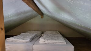 A small, attic-style bedroom with two single beds, wooden beams, and a sloped ceiling.