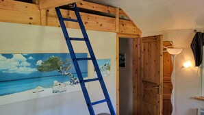 A room with a wooden ceiling, a blue ladder leaning against a wall, a gray sofa, and a painting of a beach scene.