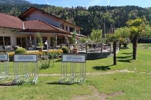 Un restaurante con terraza, rodeado de un césped cuidado y árboles, con montañas al fondo.