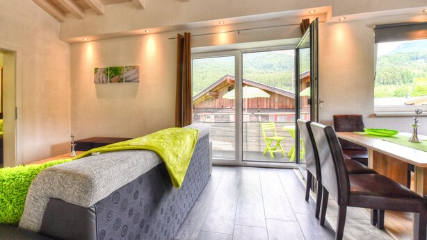 A modern room with a bed, a dining area, and a sliding glass door leading to a balcony.