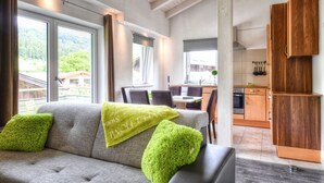 A modern living room with a sofa, green pillows, and a view of a kitchen and dining area.