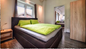 A bedroom with a bed, a nightstand, a wooden wardrobe, and a window with curtains.