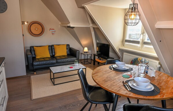 Un loft acogedor con comedor, sofá con cojines amarillos, televisor y ventana con vistas.