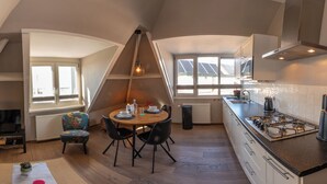 A loft-style living and dining area with a high ceiling, a fireplace, a television, a dining table with chairs, and a kitchen with a stove and sink.