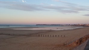 A wide beach with a wooden fence in the foreground and a cityscape in the background.