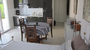 A compact kitchen with modern appliances, a dining area with a striped tablecloth, and a bed with a white comforter. - Cosy studio 2 pers.,  parking,  2 terraces,  wifi (Laroque-Des-Albères)