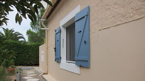 A building with a beige exterior, a window with blue shutters, and a stone pathway leading to the entrance. - Cosy studio 2 pers.,  parking,  2 terraces,  wifi (Laroque-Des-Albères)