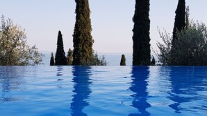 A clear view of a swimming pool with tall, slender trees in the background. - Modern apartment with Seepanoramablick in a quiet area with large infinity pool (Toscolano Maderno)