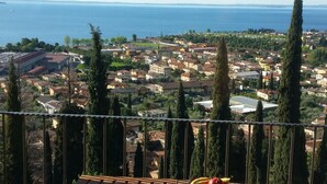 A wooden table with a book and a plate of fruit on a balcony overlooking a coastal town. - Modern apartment with Seepanoramablick in a quiet area with large infinity pool (Toscolano Maderno)
