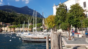 A marina with boats docked, a mountain in the background, and a white building with a balcony. - Modern apartment with Seepanoramablick in a quiet area with large infinity pool (Toscolano Maderno)