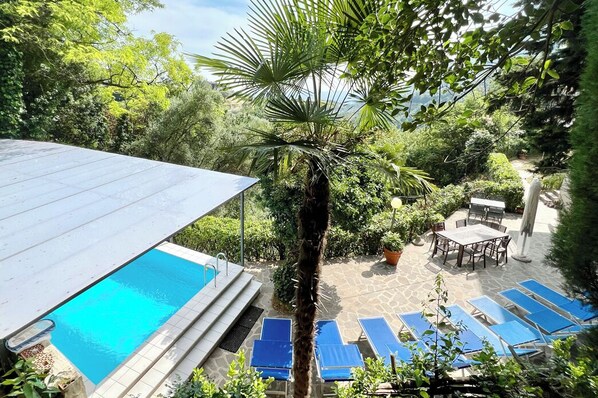 Zona de piscina con vista despejada, sillas de descanso y follaje circundante.