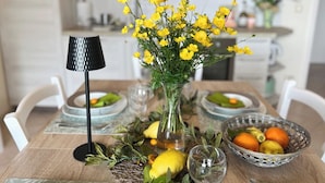 Ein Esstisch, gedeckt mit einer Vase voller gelber Blumen, einer Lampe und einem Obstkorb.
