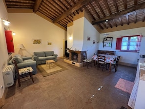 A cozy living room with a fireplace, a dining area with a table and chairs, and a red door. - Romantic comfortable house with view upon the sea, dishwasher, washing maschine (Riparbella)