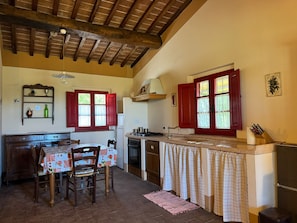 A kitchen with a wooden ceiling, a dining table with chairs, a stove, a sink, and a window with red shutters. - Romantic comfortable house with view upon the sea, dishwasher, washing maschine (Riparbella)