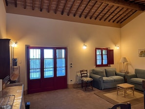 Un'ampia zona giorno con soffitto alto, una porta rossa con vetri, un divano, un tavolino e una lampada.