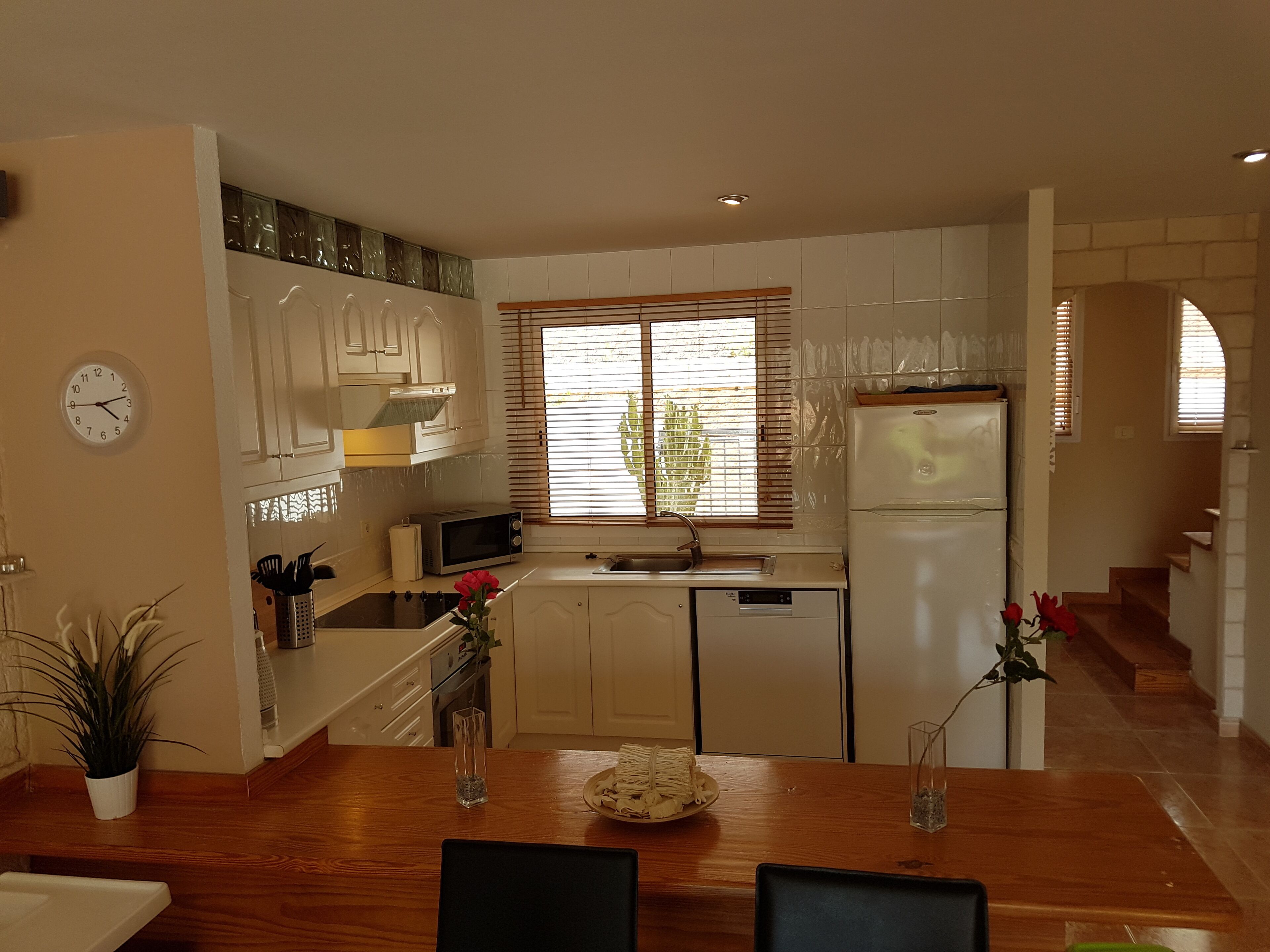 A modern kitchen with white cabinets, a microwave, a refrigerator, and a dining area with a wooden table and chairs.